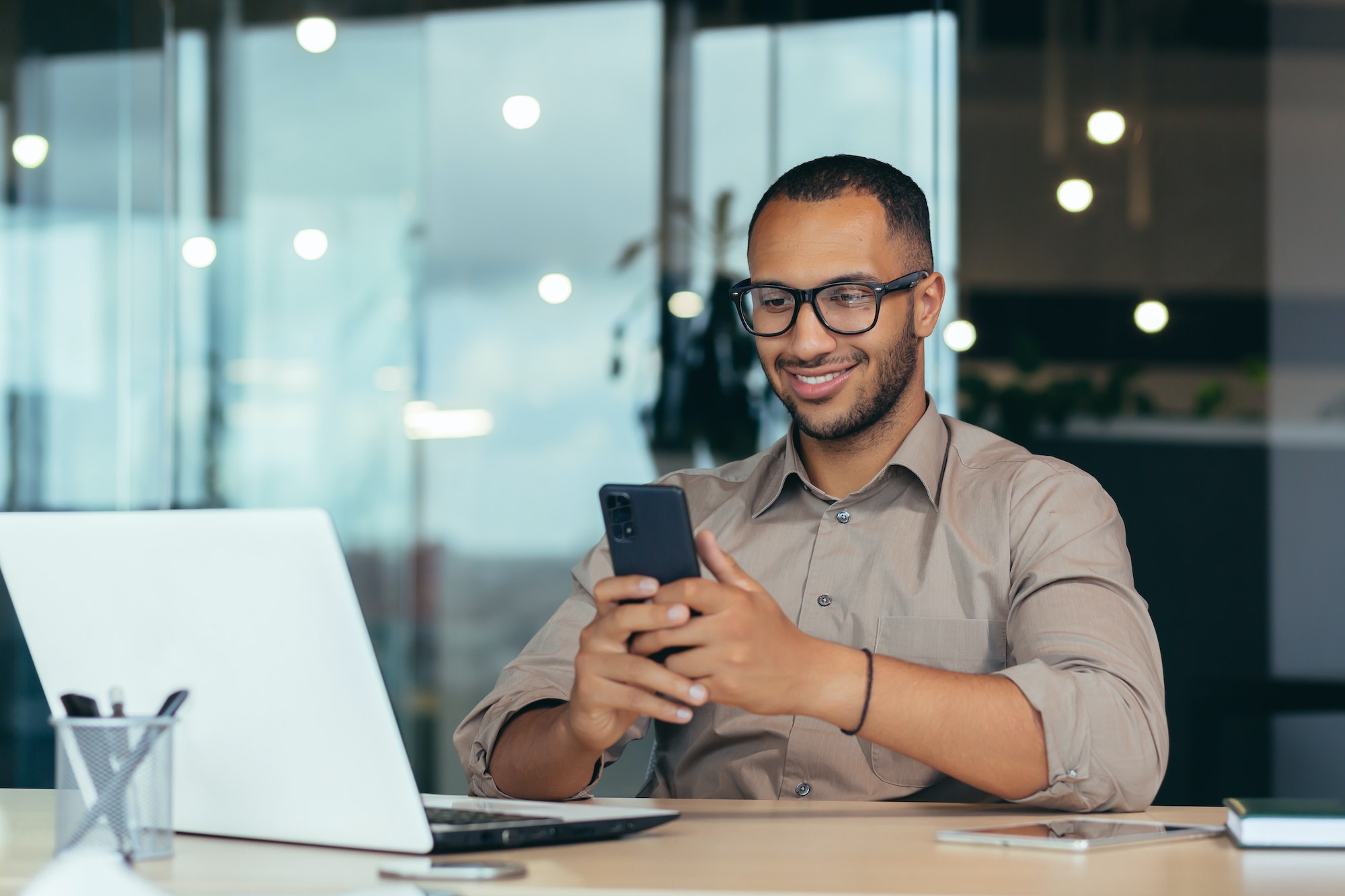 Happy african american businessman in glasses working inside modern office with laptop, man in